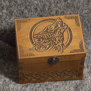 May include: A wooden box with a Celtic knot design around the edges. The lid features a carved image of a wolf howling at the moon. The box has a brass latch.