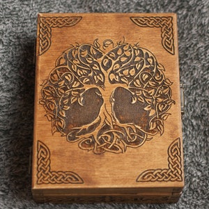 Peut inclure: Une boîte en bois avec un motif de nœud celtique autour des bords et un motif d'arbre de vie gravé au laser au centre. La boîte est en bois brun clair et a une finition naturelle.