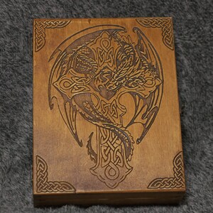 May include: A wooden box with a Celtic knot design and a dragon intertwined with the knot. The box is stained a light brown color.