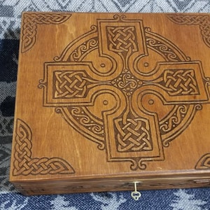 Könnte beinhalten: Eine Holzkiste mit einem geschnitzten keltischen Knotenmuster auf dem Deckel. Die Kiste ist dunkelbraun gebeizt und hat ein Messing-Schlüsselloch.