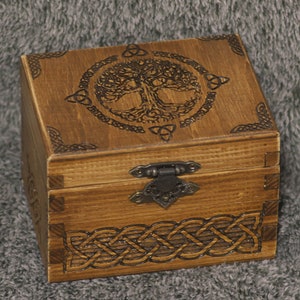 May include: A wooden box with a hinged lid and a metal latch. The top of the box is decorated with a Celtic knot design and a tree of life motif. The bottom of the box is decorated with a Celtic knot design.