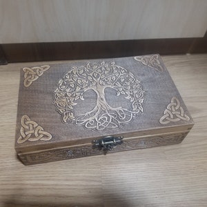 May include: A wooden box with a Celtic knot design and a tree of life engraved on the lid. The box has a metal latch.