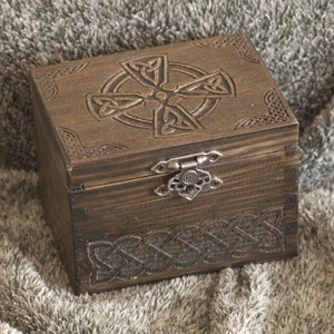 May include: A wooden box with a Celtic knot design carved into the lid and sides. The box has a metal latch and is closed.