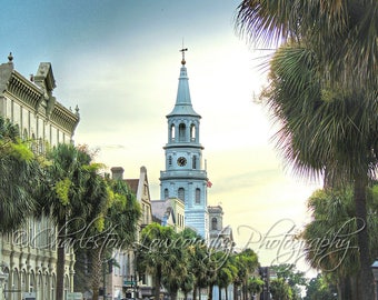 May include: A view down a street lined with palm trees in Charleston, South Carolina. A white steeple church with a clock tower is visible in the distance.