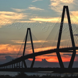 May include: Silhouette of the Arthur Ravenel Jr. Bridge in Charleston, South Carolina, against a vibrant orange and pink sunset sky.