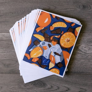 May include: A stack of white cards with a colourful illustration of oranges and chocolate on a blue background.