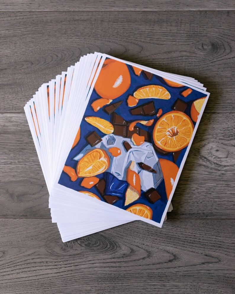 May include: A stack of white cards with a colourful illustration of oranges and chocolate on a blue background.