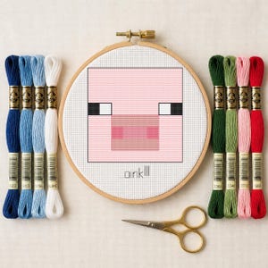 May include: A cross-stitch project in a round wooden hoop featuring a pixelated pink pig face and the text oink!!!, accompanied by eight skeins of embroidery floss in shades of blue, white, green, pink, and red, and a pair of gold scissors.
