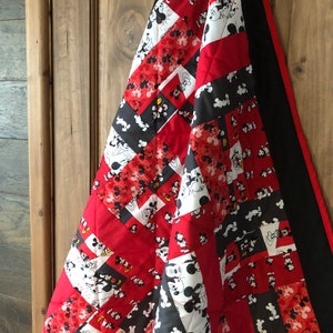 May include: A red and black quilt featuring a Mickey Mouse design. The quilt is made from various fabrics and has a black border.