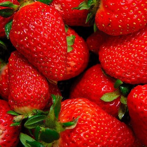 Puede incluir: Una imagen de primer plano de un tazón lleno de fresas rojas maduras. Las fresas están dispuestas en un patrón aleatorio, con algunas superpuestas. Las fresas son brillantes y tienen un aspecto brillante.