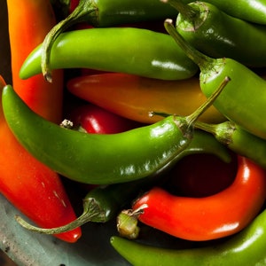 May include: A close-up of a variety of chili peppers, including red, orange, and green. The peppers are arranged in a bowl and are ready to be used in cooking.