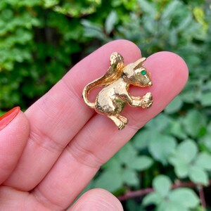 May include: A gold-toned mouse brooch with a green rhinestone eye. The mouse is sitting on its hind legs and holding a small object in its paws.