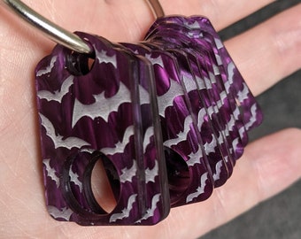 May include: A set of purple keychains with a bat pattern. The keychains are attached to a silver ring.
