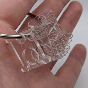 May include: A clear acrylic keyring with a decorative design. The keyring is attached to a silver metal ring.