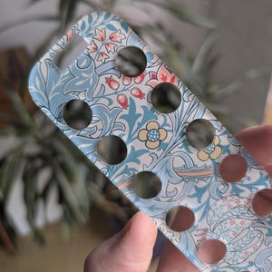 May include: A clear phone case with a floral pattern in shades of blue, pink, and white. The case has multiple circular cutouts.