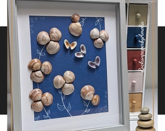 May include: A framed artwork featuring a blue background with white floral designs and seashells arranged to look like flowers. The artwork is titled "RocksnpaperbyAmelia".