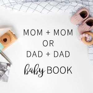 May include: A white surface with a pink baby shoe, a wooden teething ring, a wooden camera, a pen, two black and white baby photos, and a white and black checkered fabric. The text on the surface reads 'MOM + MOM OR DAD + DAD baby BOOK'.