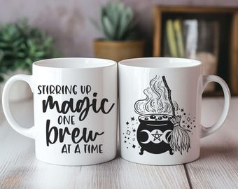 May include: Two white ceramic mugs with black text and images. The mug on the left says "Stirring up magic one brew at a time". The mug on the right has a black and white illustration of a cauldron with steam rising from it, a broom, and a triple moon symbol.