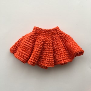 Puede incluir: Una falda de crochet de color naranja brillante con un dobladillo con volantes.