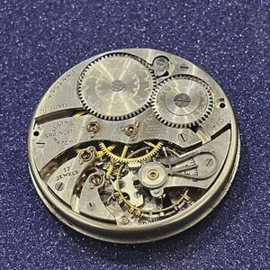 Puede incluir: Primer plano de un movimiento de reloj Illinois Springfield vintage. El mecanismo de esfera abierta presenta intrincados engranajes, joyas y el texto "17 Jewels". El reloj est&aacute; marcado como "Adjusted" y tiene el n&uacute;mero de serie 4951443.