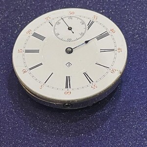 May include: A vintage pocket watch with a white face, black Roman numerals, and red minute markers. The watch has a small subdial and a silver-colored metal casing. The hands are black and blue.