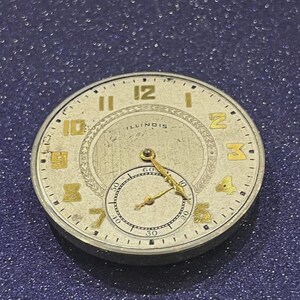 Puede incluir: Una esfera de reloj vintage con n&uacute;meros y manecillas doradas sobre un fondo color crema. La palabra "ILLINOIS" es visible en el centro. La esfera del reloj tiene una esfera secundaria m&aacute;s peque&ntilde;a en la parte inferior.