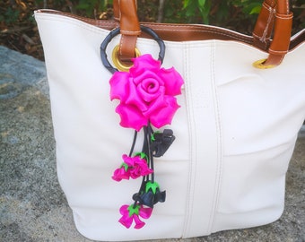 May include: A white tote bag with brown leather handles and a pink and black flower charm attached to the handle.