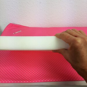 May include: A white foam pipe insulation tube on a pink fabric with white polka dots.