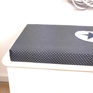 May include: White storage bench with a dark gray padded seat featuring a white polka dot pattern. The seat has a white star-shaped patch.