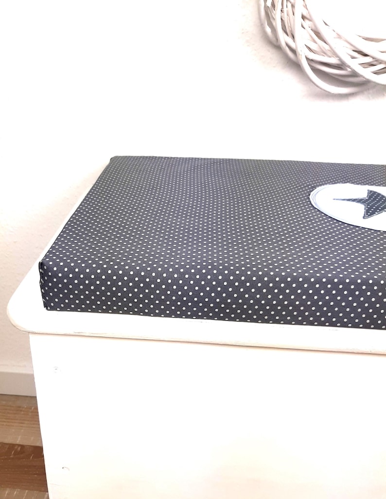 May include: White storage bench with a dark gray padded seat featuring a white polka dot pattern. The seat has a white star-shaped patch.