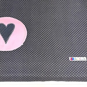 May include: A black changing pad with white polka dots and a pink circle with a black heart in the center. The changing pad has a white label that says "Handmade".