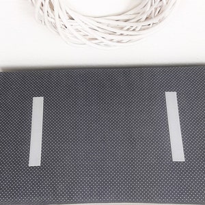 May include: A dark gray fabric with white polka dots. Two white strips of tape are attached to the fabric, one on each side.