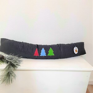 Könnte beinhalten: Ein schwarzer und weißer Türdämpfer in Form eines langen Kissens mit drei Filz-Weihnachtsbäumen in Rot, Blau und Grün.