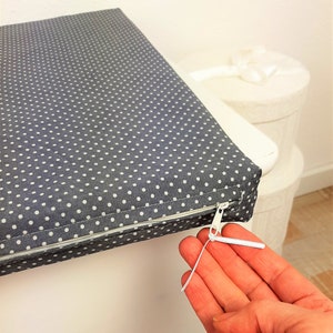 May include: A gray and white polka dot cushion with a zipper closure. The zipper pull is white and has a metal slider.