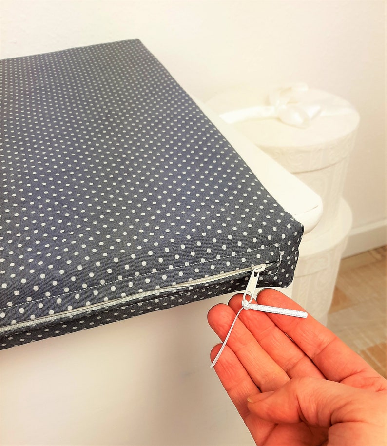 May include: A gray and white polka dot cushion with a zipper closure. The zipper pull is white and has a metal slider.