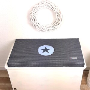 May include: A white wooden storage box with a gray and white polka dot cushion top. The cushion has a blue star in a circle in the center.