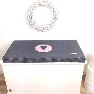 May include: A white toy chest with a dark blue and white polka dot lid. The lid has a pink circle with a dark blue heart in the center.