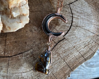 May include: A copper chain necklace with a black crescent moon pendant and a tiger's eye wolf pendant.