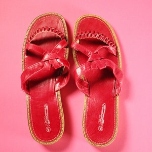May include: A pair of red leather sandals with a woven strap design. The sandals have a brown leather sole and are labeled "Hawaiian" on the bottom.