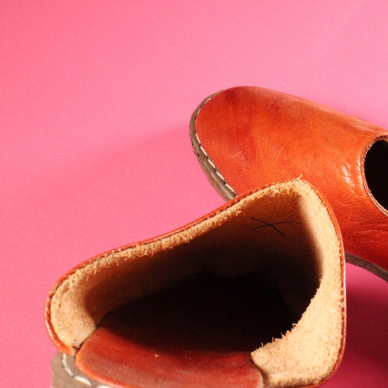 May include: Two brown leather shoes with a stitched seam around the edge. The shoes are turned inside out, showing the soft brown lining.