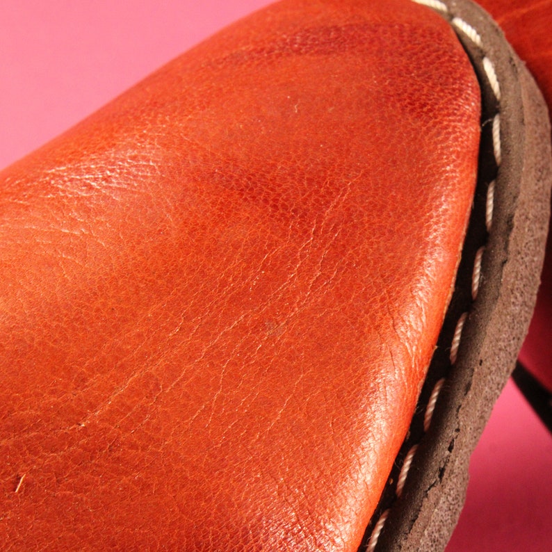 May include: Close-up of a brown leather surface with a white stitching detail. The leather has a textured, grainy appearance.