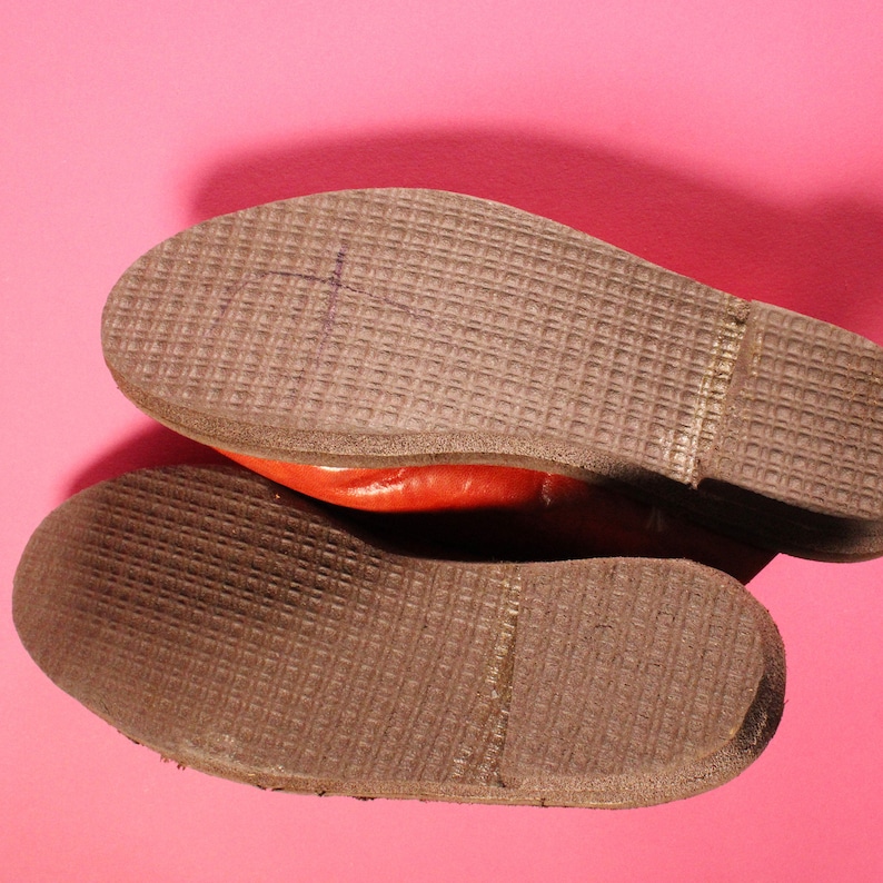 May include: Close-up of the brown leather soles of a pair of red leather shoes. The soles have a textured pattern.