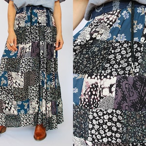 Può includere: Lunga gonna patchwork con una varietà di motivi floreali e paisley nei toni del blu, nero, bianco e viola. La gonna ha una vita con coulisse e viene indossata con stivali marroni.