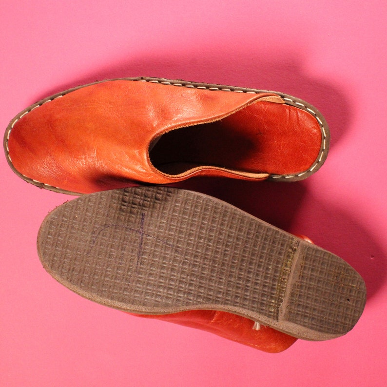Op de afbeelding: Vintage 1970s Handgemaakte Deadstock Indiase loafers muiltjes instappers. Een paar bruine leren slippers met een gestikte naad rond de rand. De slippers hebben een bruin leren bovenwerk en een bruine rubberen zool.
