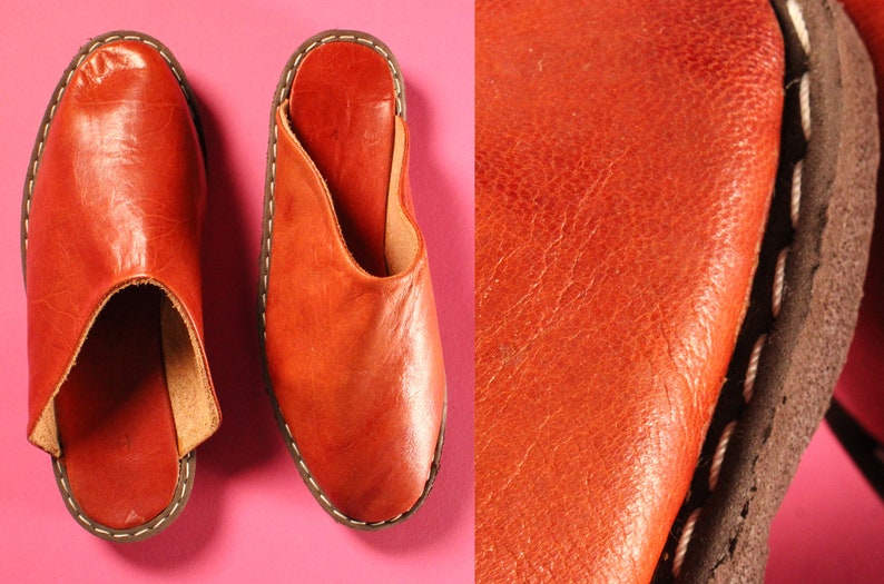 Op de afbeelding: Vintage 1970s Handgemaakte Deadstock Indiase loafers muiltjes instappers. Een paar bruine leren slippers met een gestikte rand. De slippers hebben een ronde neus en een open achterkant.