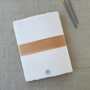 May include: A white sheet of paper with a deckled edge and a brown ribbon tied around it. The paper has a watermark that says "The Source of Paper Goods".