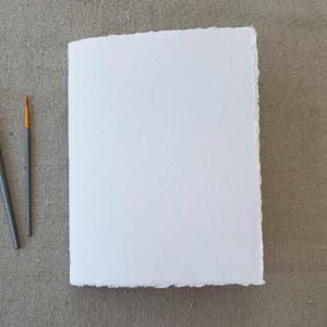 May include: A white sheet of paper with a deckled edge, perfect for painting or drawing. Two paintbrushes are visible on the left side of the image.