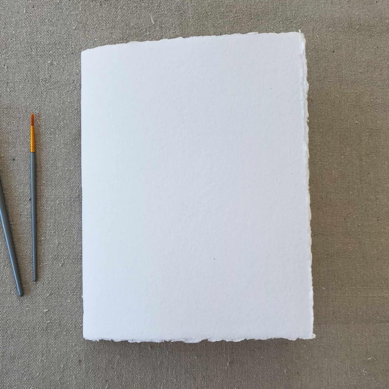 May include: A white sheet of paper with a deckled edge, perfect for painting or drawing. Two paintbrushes are visible on the left side of the image.
