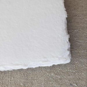 May include: A sheet of white handmade paper with a rough, textured surface and deckled edges.