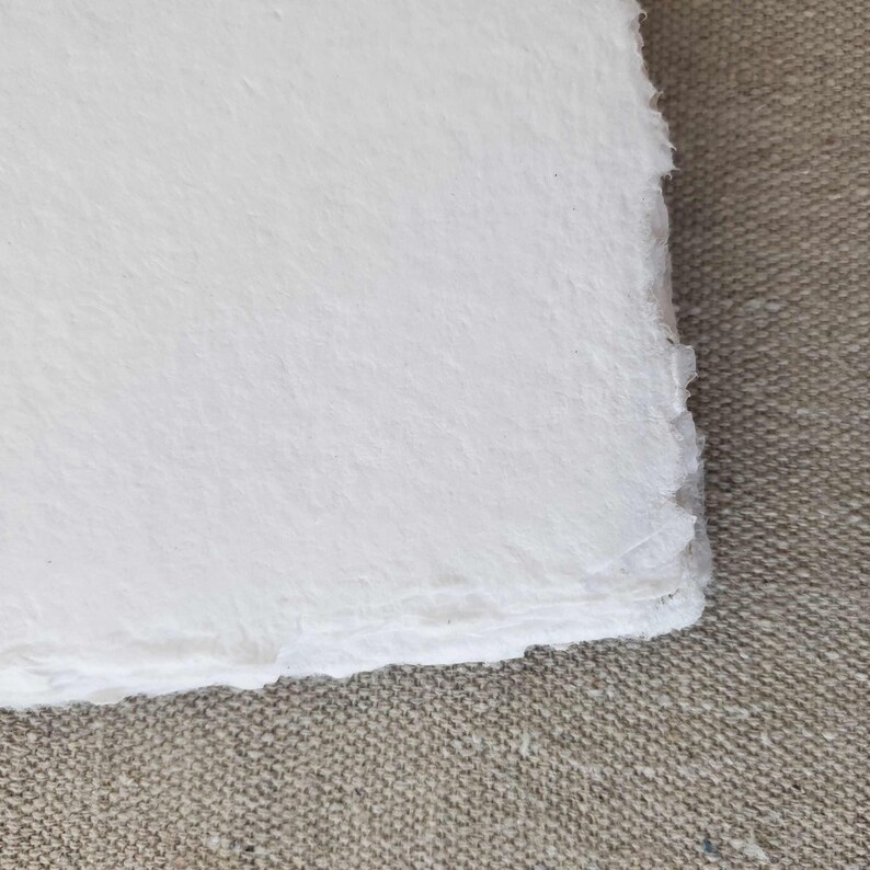 May include: A sheet of white handmade paper with a rough, textured surface and deckled edges.